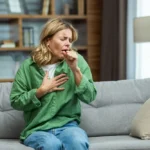 a woman sitting on a couch holding her hand to her chest / How to Test Your Home for Allergens and Improve Air Quality // Signs That Allergens Might Be in Your Home // Common Indoor Allergens That Affect Air Quality // How to Test for Allergens in Your Home // When to Get Professional Allergen Testing // Common Areas to Check for Allergens // Understanding and Responding to Test Results // How to Reduce Allergens in Your Home // Keep Your Home’s Air Allergen Free // ETA Mold Mold Testing and Air Quality Services in Florida