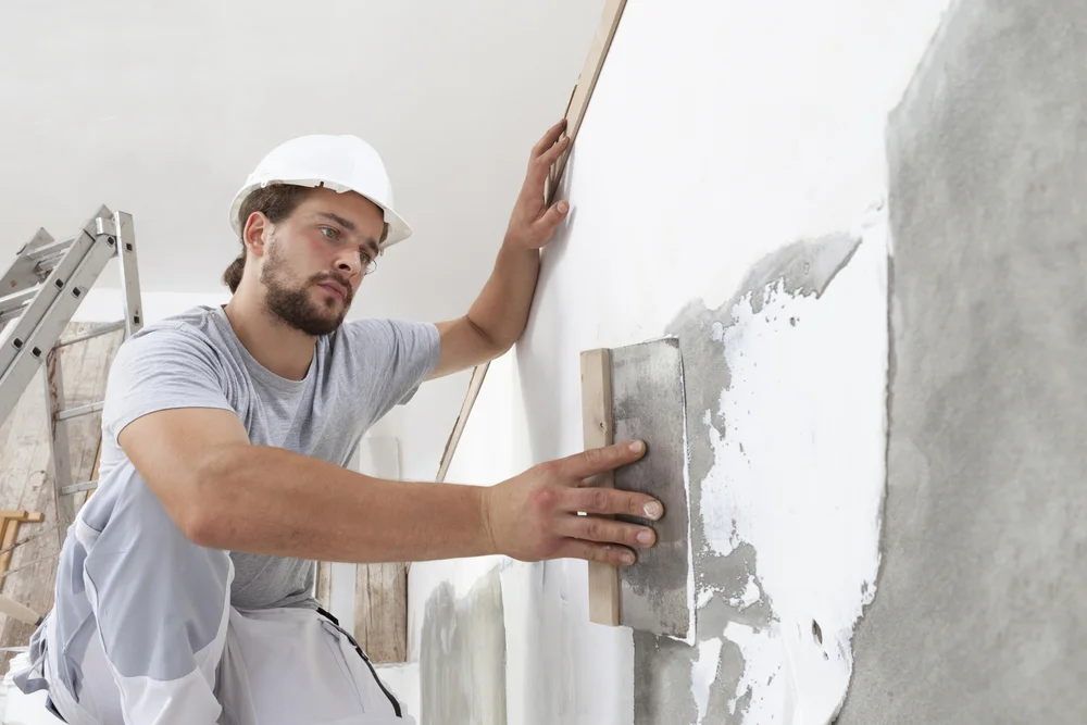 a man in a hard hat using a trowel to put plaster on a wall / A Complete Guide to Mold-Resistant Products for Your Home / What Are Mold-Resistant Products? / How Do Mold-Resistant Products Work? / Mold-Resistant Products For Your Home / Mold-Resistant Drywall / Mold-Resistant Paint / Mold-Resistant Insulation / Mold-Resistant Flooring / Mold-Resistant Caulk / Dehumidifiers / Mold-Resistant Fabrics / Benefits of Using Mold-Resistant Products / How to Maintain Mold-Resistant Products / When to Call a Mold Inspection & Testing Expert / FAQs About Mold-Resistant Products / ETA Mold Inspection and Testing in Florida