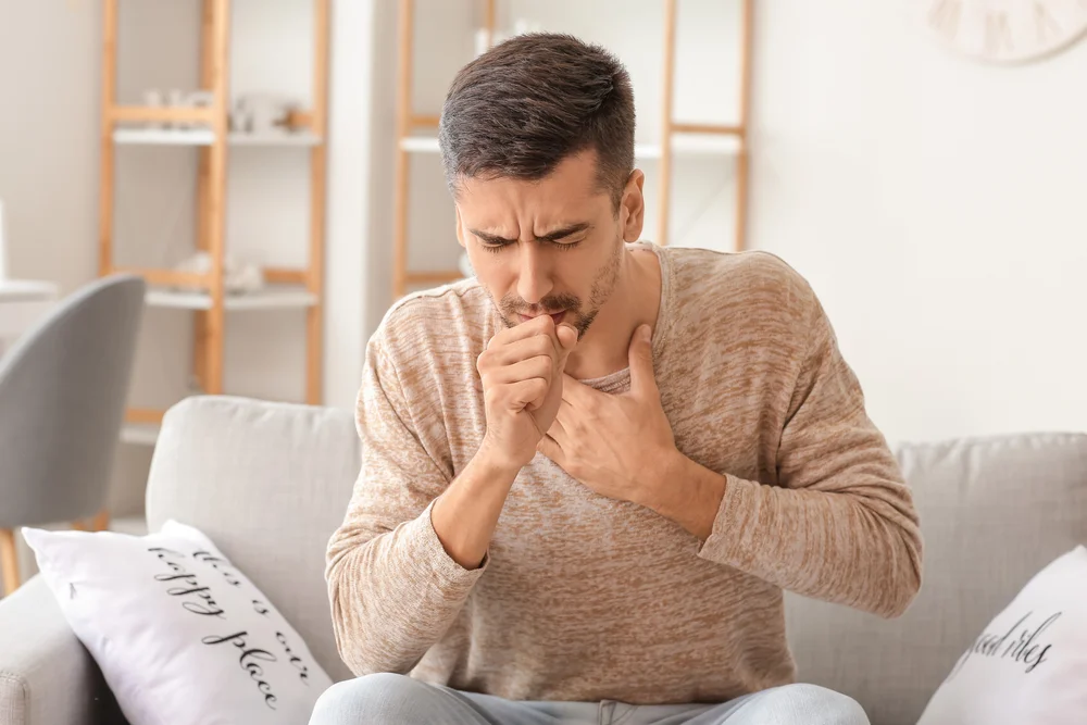 a man sitting on a couch with his hands in his mouth / Mold and Respiratory Problems: What Every Floridian Needs to Know / What Is Mold, and How Does It Affect Your Lungs? / Common Types of Mold That Affect the Lungs / Symptoms of Mold-Related Respiratory Issues / How Mold Exposure Is Diagnosed / Treatment for Mold-Related Respiratory Issues / Preventing Mold in Your Florida Home / Protecting Your Health from Mold in Florida