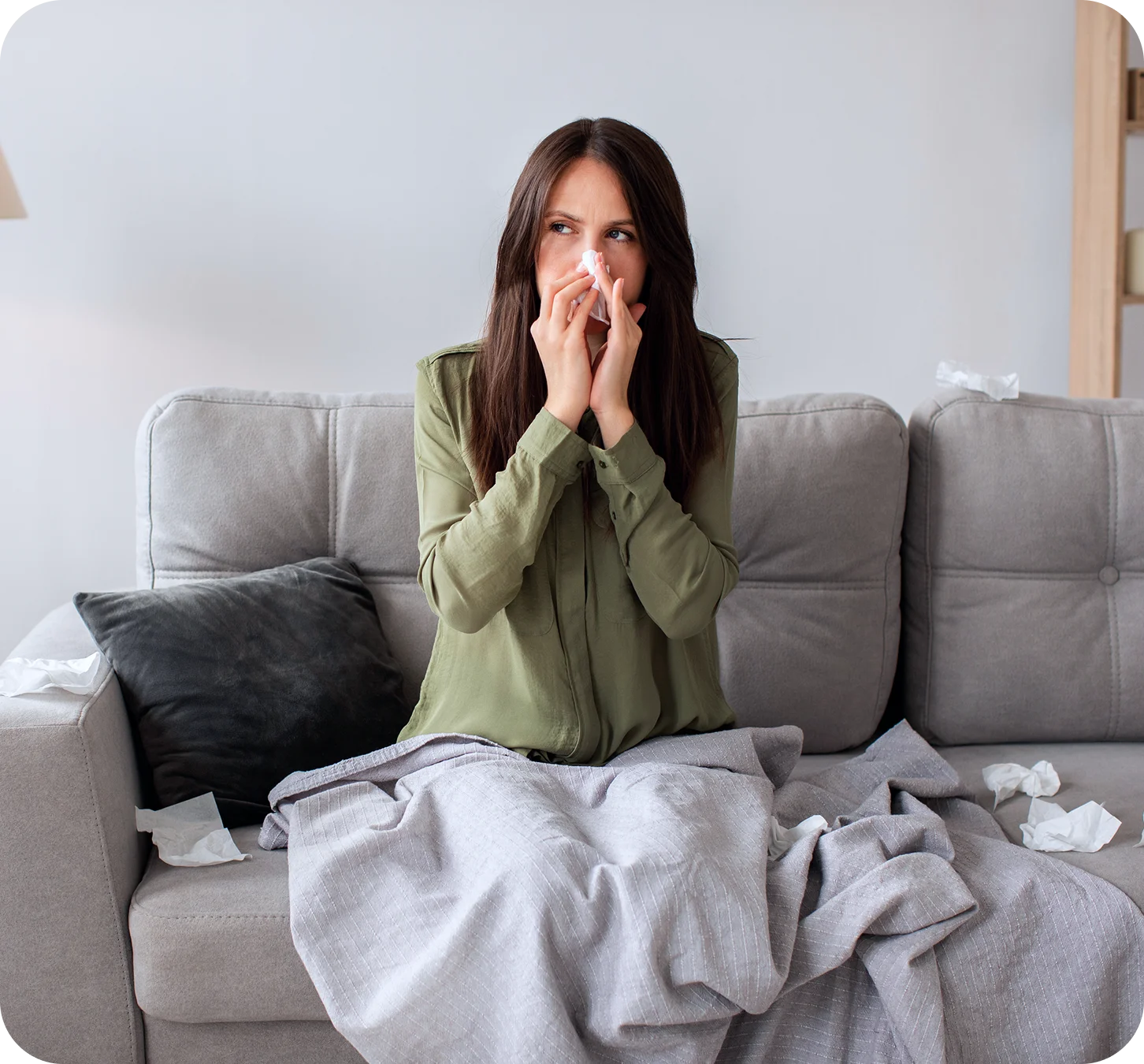 Woman sitting on couch blowing her nose with a tissue