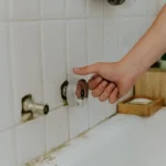 hand turning bathroom faucet in white tiled room - How to Clean Shower Mold?